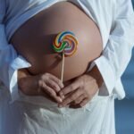 closeup pregnant female holding lollipop near her belly sunlight