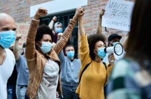 multiethnic crowd people with protective face masks protesting city streets focus is african american women holding hands